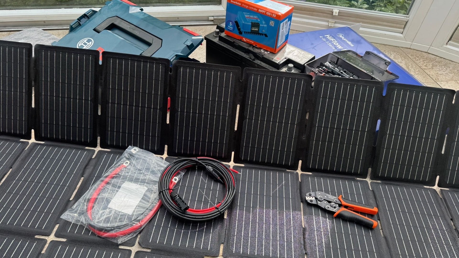 Eingetroffene Komponenten meines DIY-Solar-Setups: mehrere faltbare ECTIVE-Solarmodule ausgelegt, ein Victron-MPPT-Laderegler im Karton, MC4-Solarkabel im Beutel und eine MC4-Crimpzange — fertig sortiert vor dem Zusammenbau.